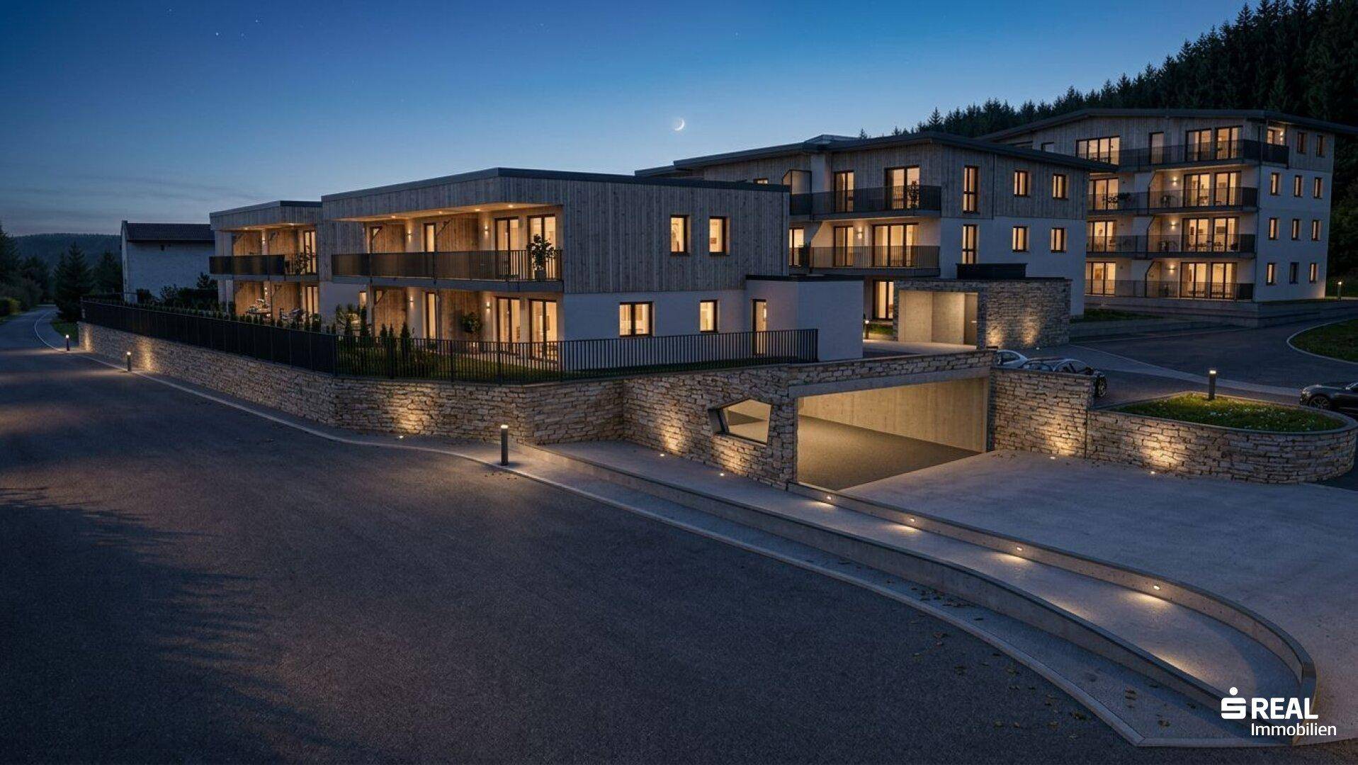 Beleuchtete Wohnanlage bei Nacht mit Tiefgaragenzufahrt und moderner Architektur.