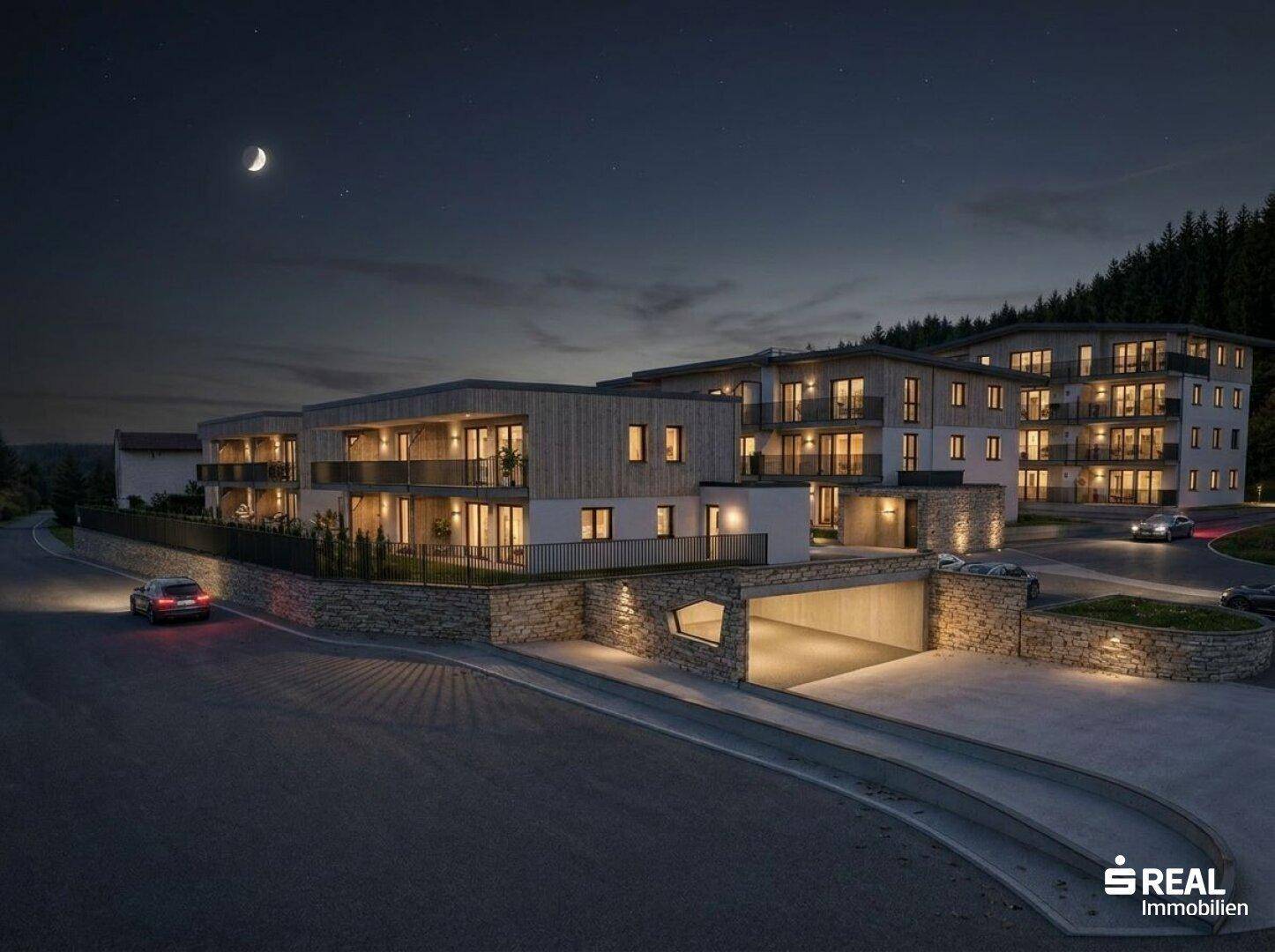 Die moderne Wohnanlage bei Nacht, beleuchtet und eingebettet in die natürliche Umgebung.