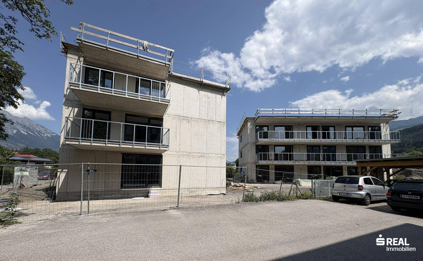 Zwei Neubaugebäude im Rohbau mit Balkonen und Bergblick unter klarem Himmel.
