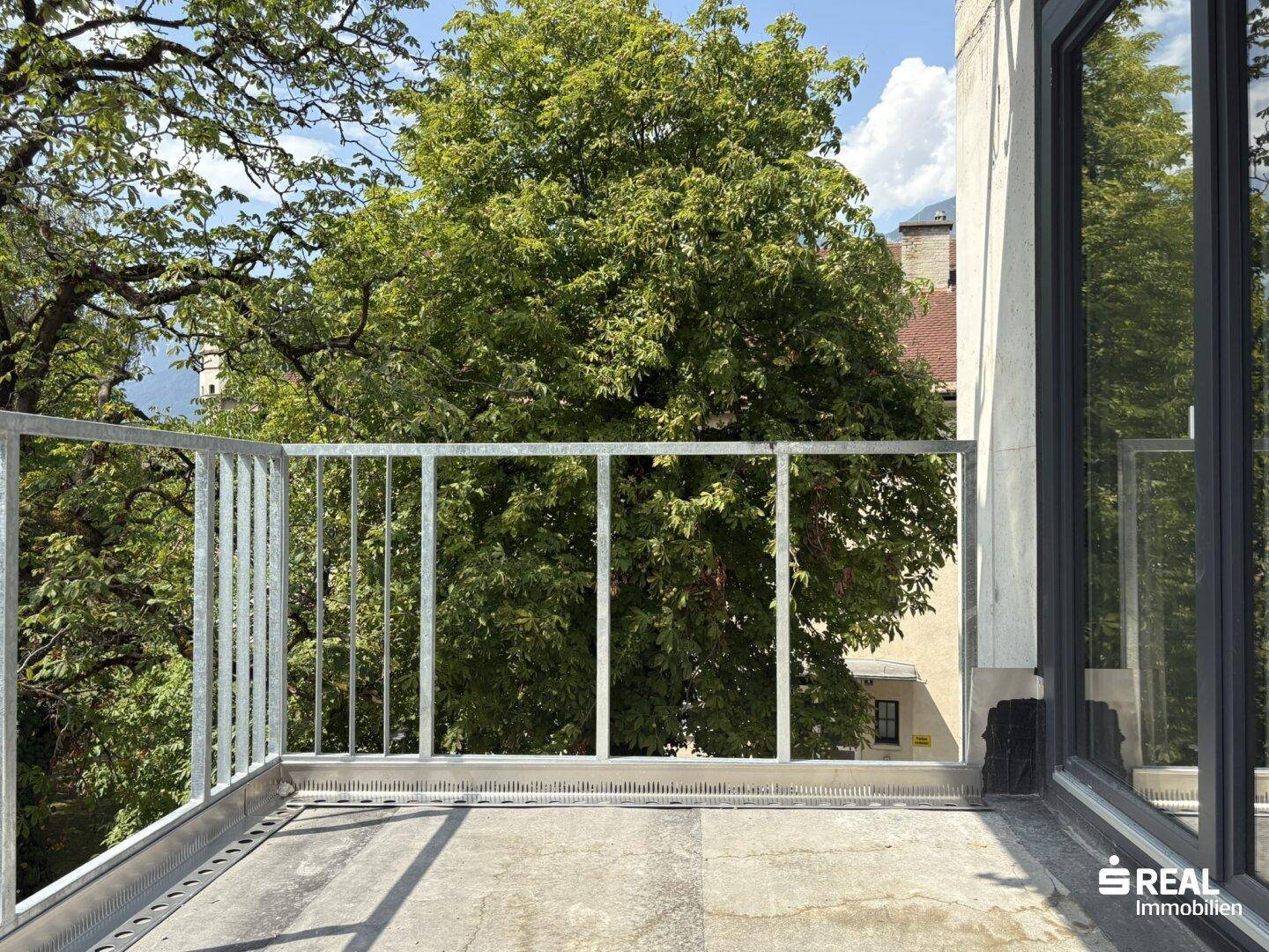 Unfertiger Balkon mit Metallgeländer und weitem Blick auf grüne Bäume und die Umgebung.