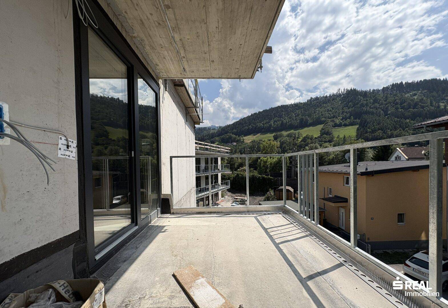 Unfertiger Balkon mit Metallgeländer und weitem Blick auf grüne Hügel und die Umgebung.