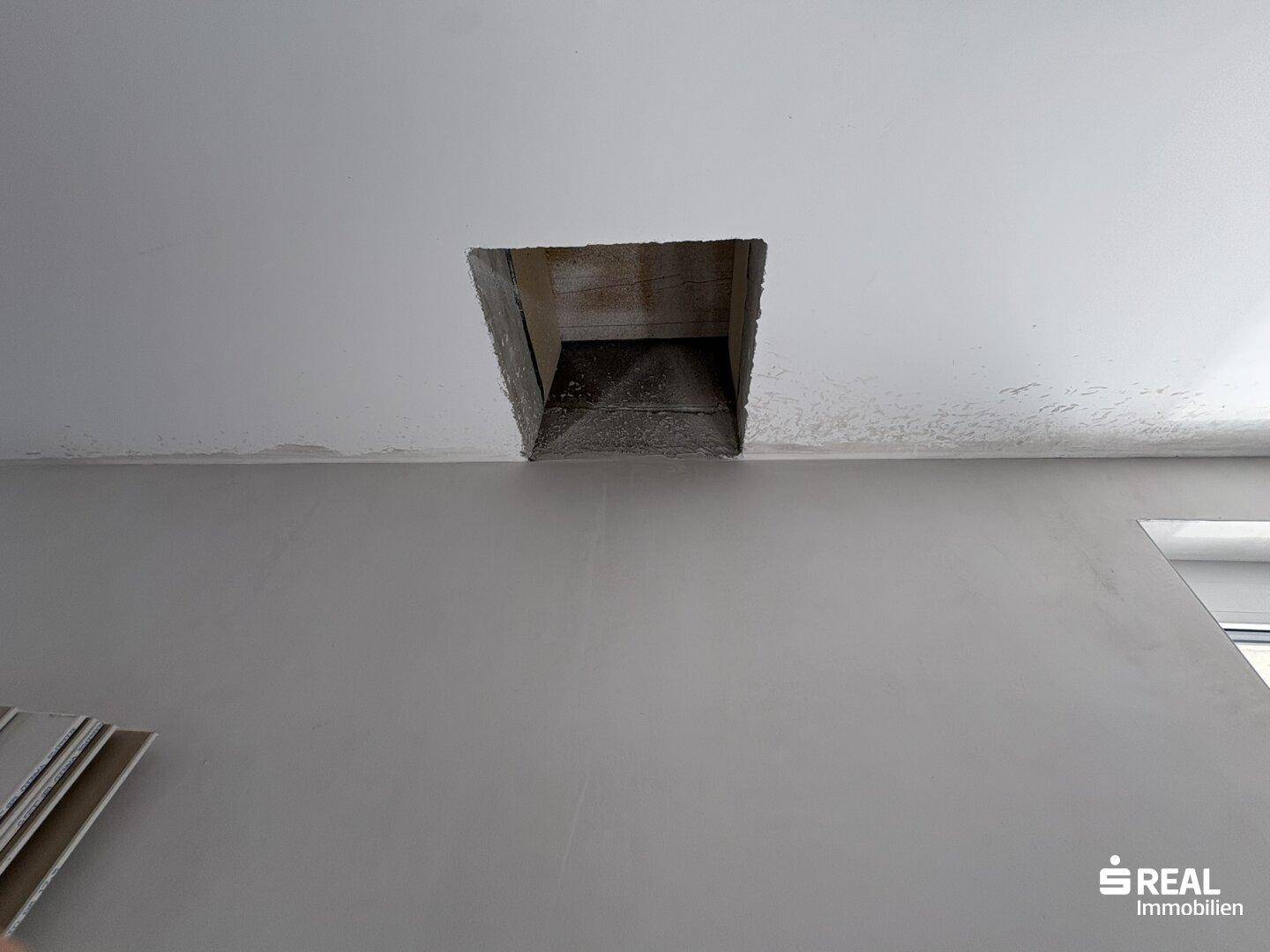 Innenraum mit grauen Wänden und einer rechteckigen Öffnung in der Decke, möglicherweise für Belüftung.