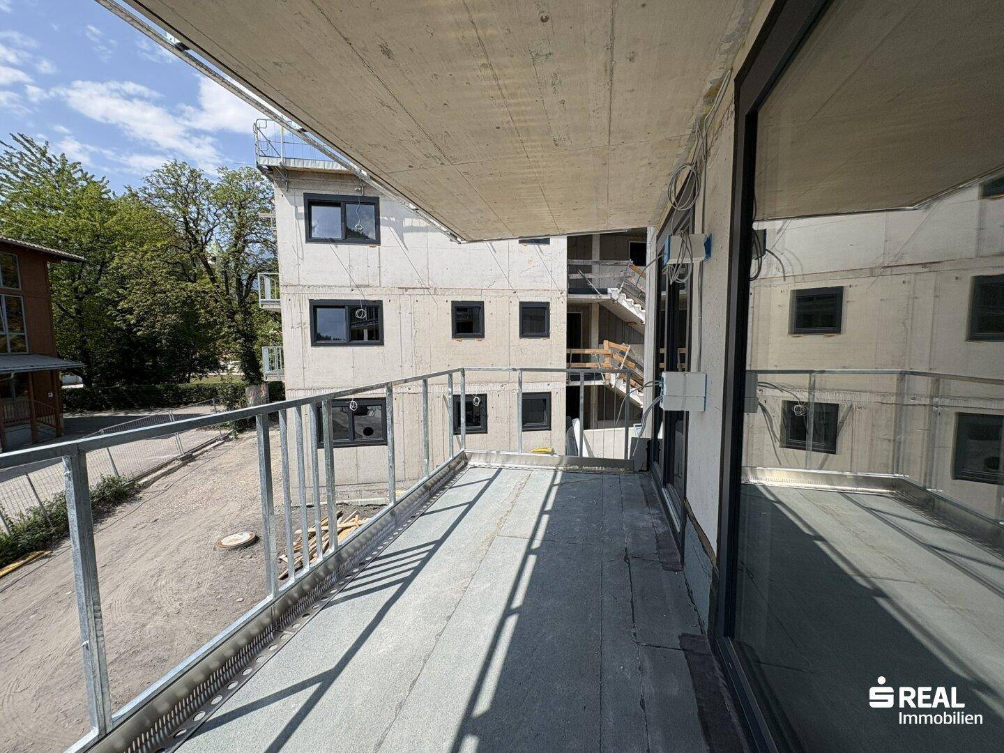 Langer Balkon eines Neubaus mit Glasgeländer und Blick auf die grüne Umgebung.