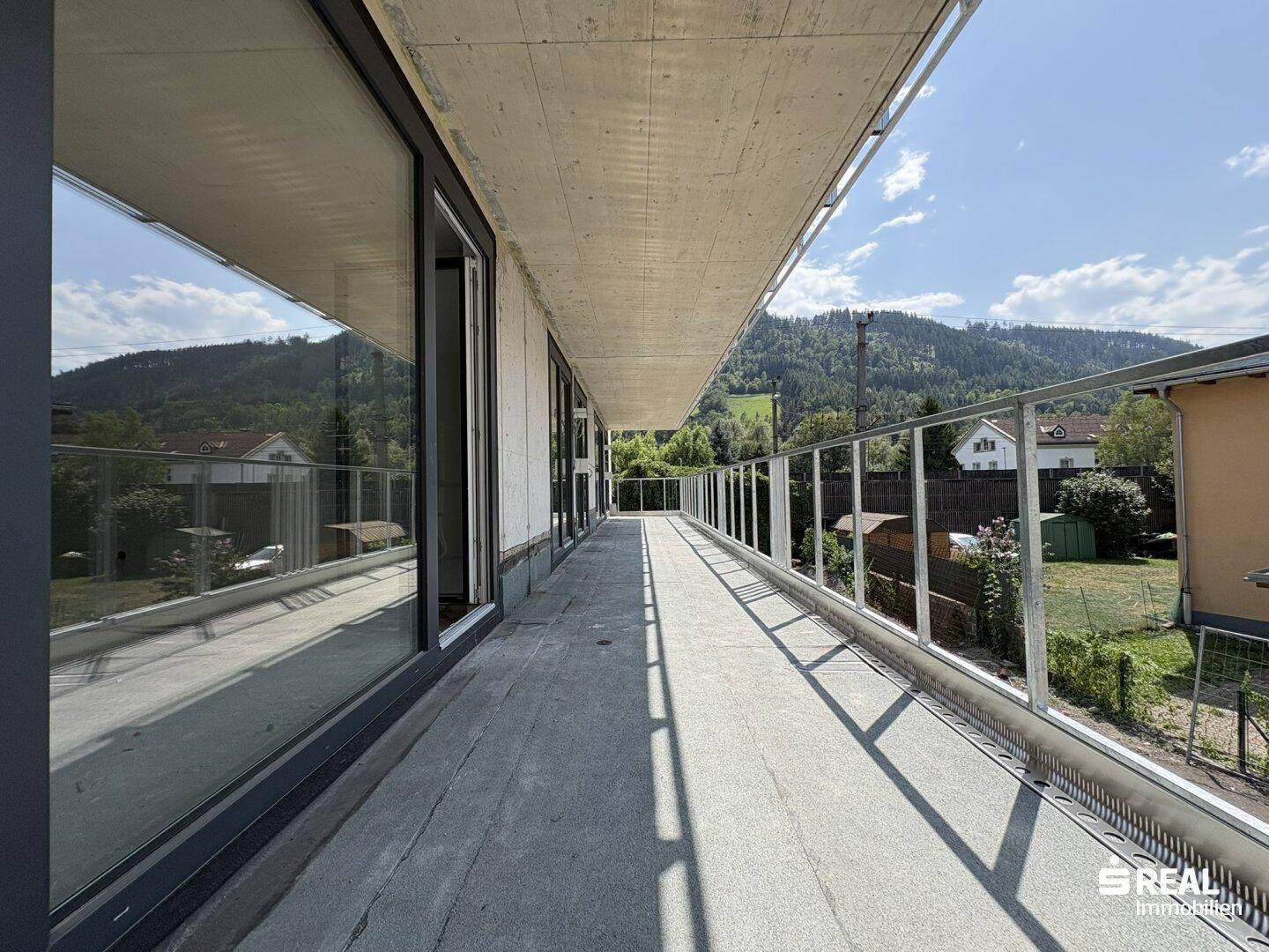 Geräumiger Balkon mit Glasgeländer und weitem Blick auf die umliegende Berglandschaft.