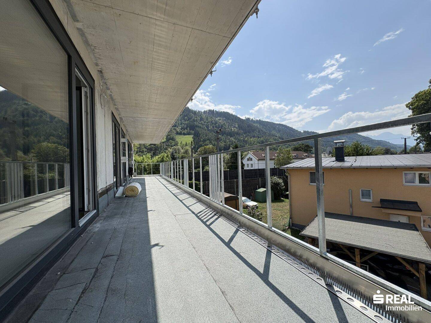 Langer Balkon mit moderner Glasbrüstung und weitem Blick auf die bewaldeten Hügel.