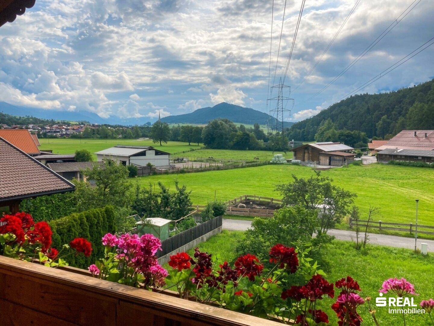 Balkon mit bunten Blumenkästen und weitem Blick auf die grüne Landschaft und Berge.