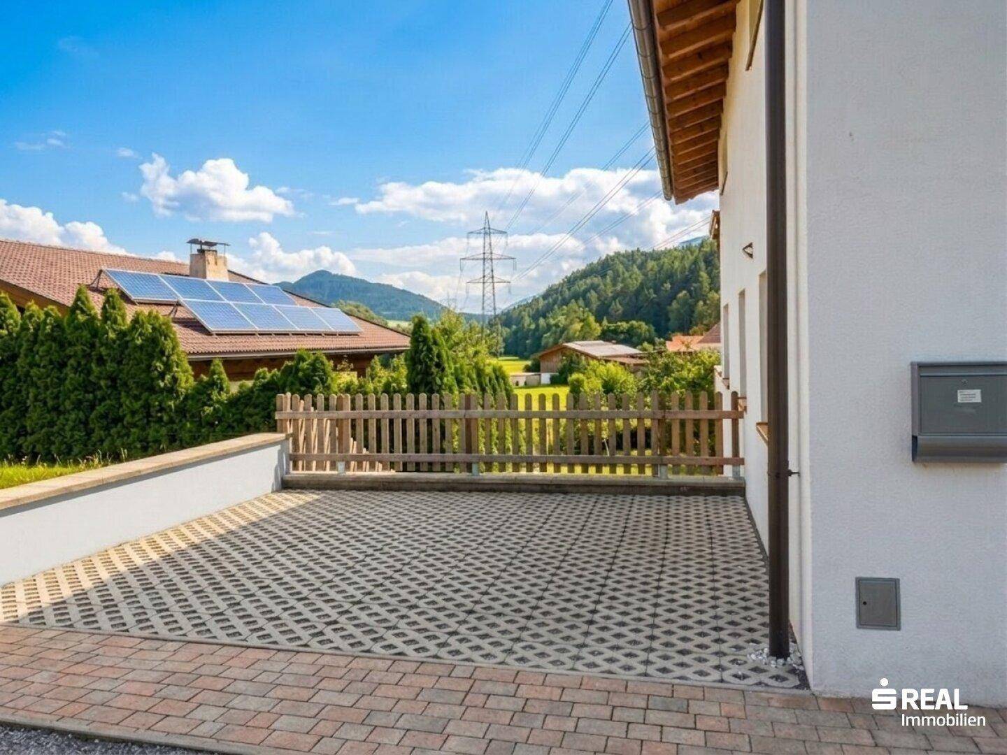 Außenbereich mit gepflastertem Parkplatz und Blick auf ein Nachbarhaus mit Solaranlage.