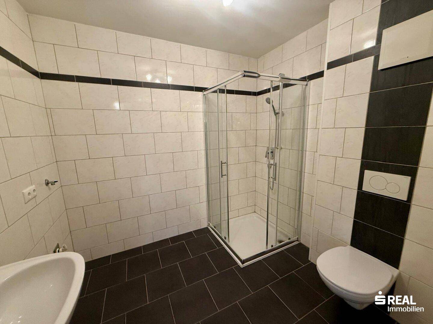 Modernes Badezimmer mit Duschkabine, weißen und schwarzen Fliesen und WC.