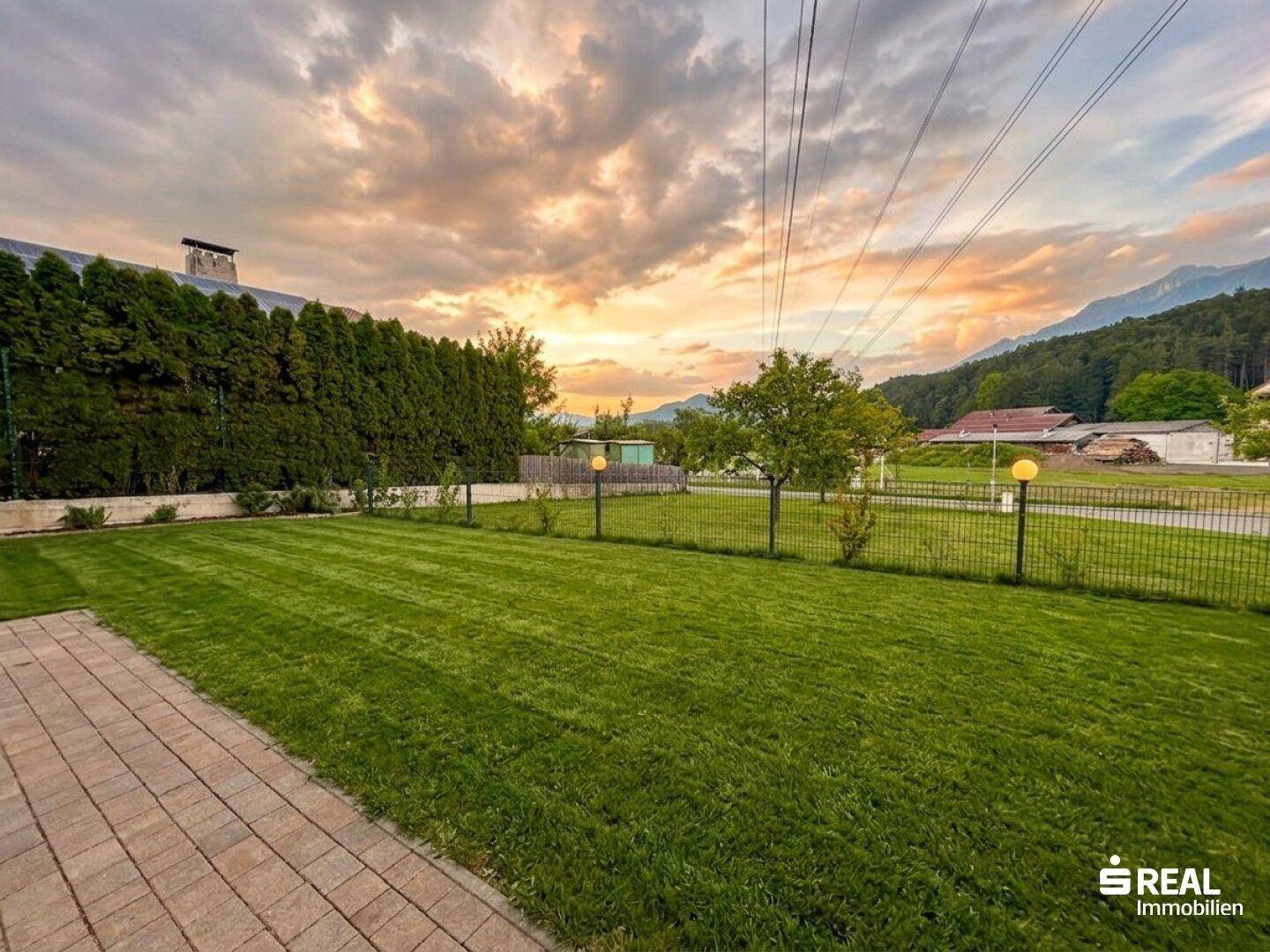 Gepflegter Rasenbereich mit gepflastertem Weg und Blick auf die umliegende Landschaft bei Sonnenuntergang.