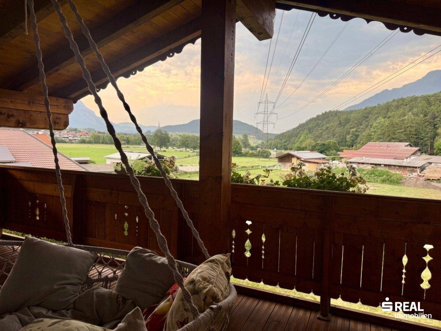 Gemütlicher Holzbalkon mit Hängesessel und weitem Blick auf die Berge und Landschaft.
