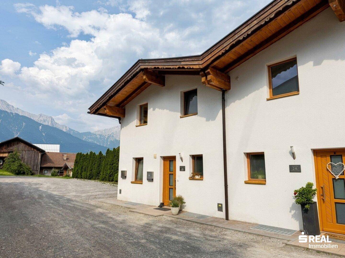 Traditionelles Haus mit Holztüren und Bergblick unter einem bewölkten Himmel.