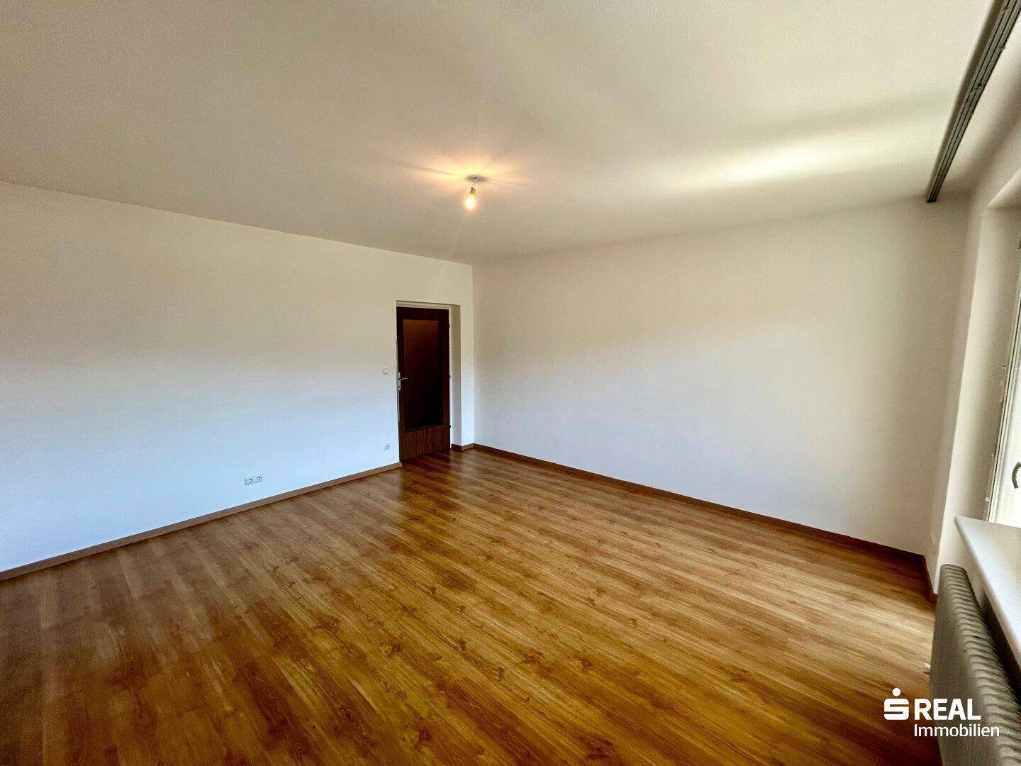 Geräumiges Wohnzimmer mit Laminatboden und weiß gestrichenen Wänden, bereit zur individuellen Gestaltung.