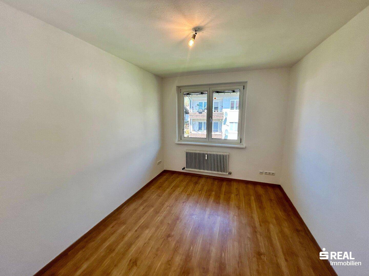Schlafzimmer mit Laminatboden, Fenster und Heizkörper, ideal für ein Kinder- oder Gästezimmer.