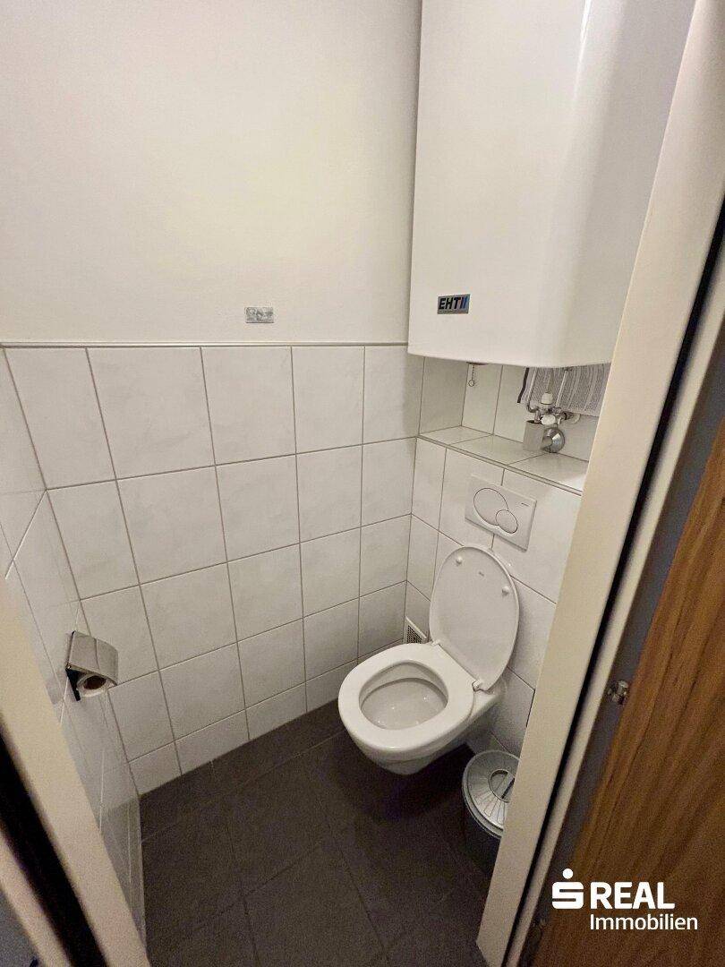 Separates WC mit Toilette, Wandfliesen und Warmwasserboiler, praktisch für Gäste.