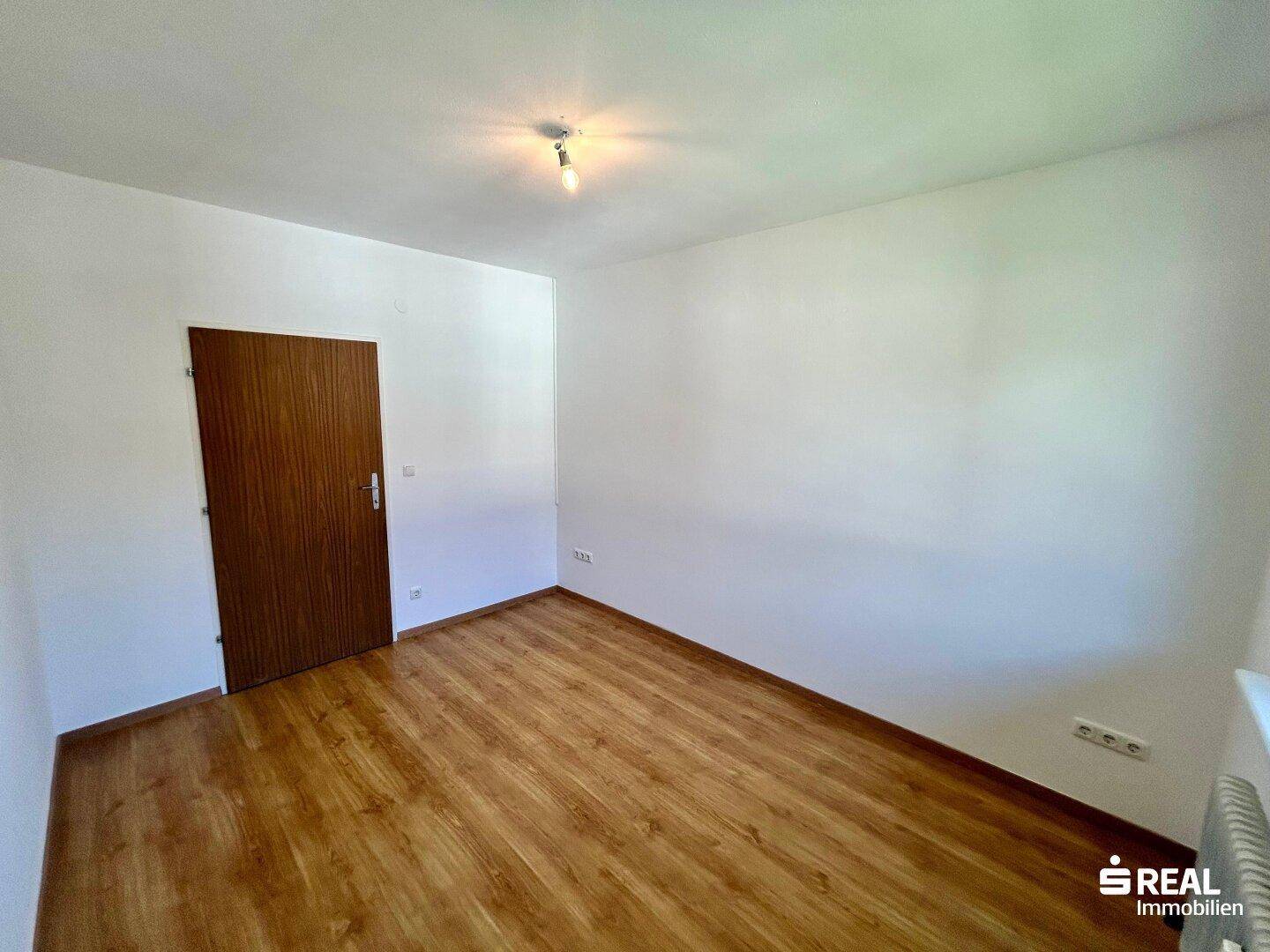 Helles Zimmer mit Laminatboden und schlichter Einrichtung, bietet viel Potenzial für persönliche Gestaltung.