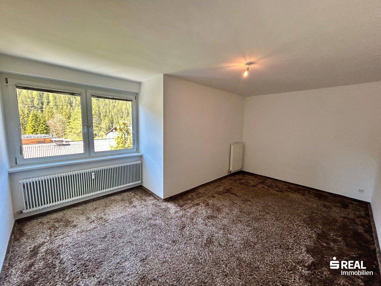 Gemütliches Schlafzimmer mit Teppichboden und Fenster mit Blick auf die umliegende Natur.