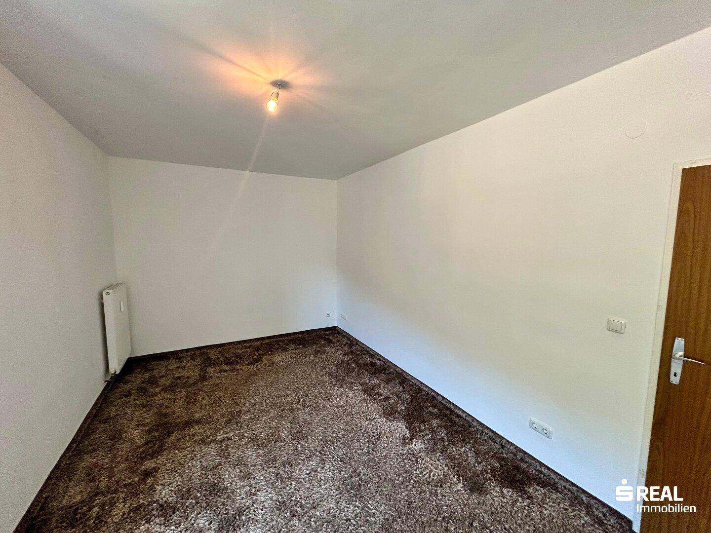 Geräumiges Schlafzimmer mit braunem Teppichboden und weiß gestrichenen Wänden, bietet viel Platz.