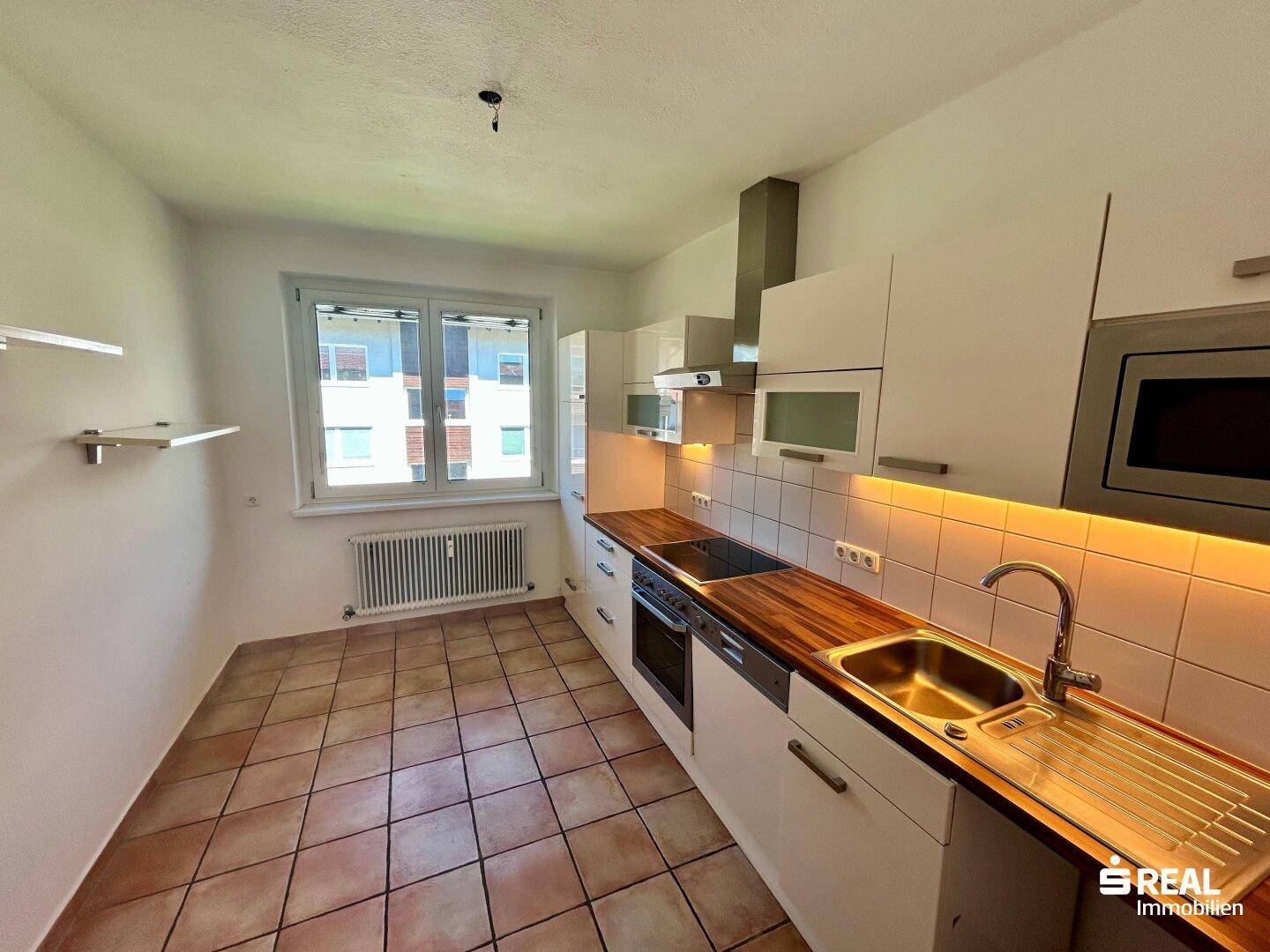 Helle Küche mit Fenster, weißen Oberschränken und Terrakotta-Fliesenboden, bietet ausreichend Arbeitsfläche.