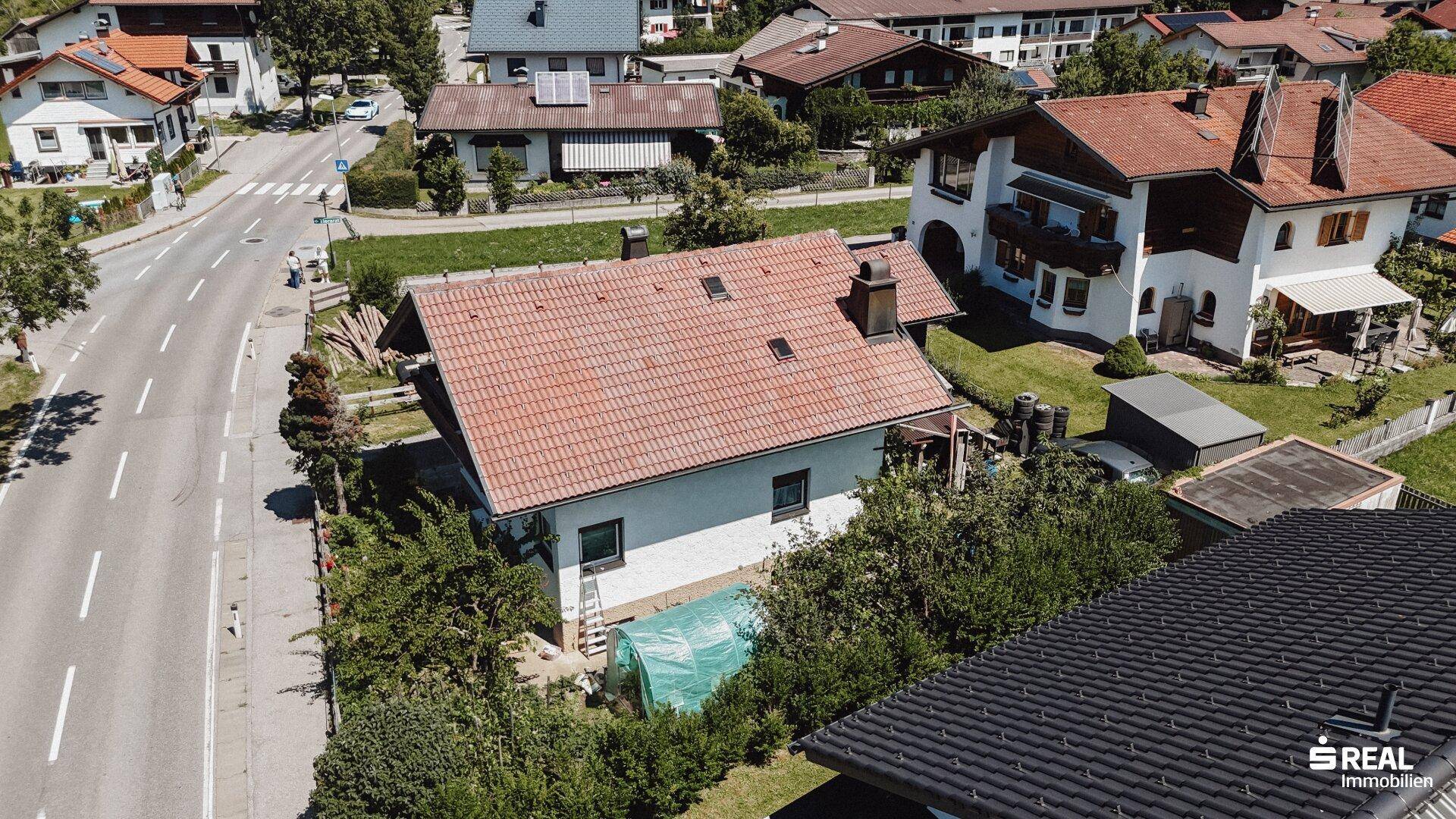 Vogelperspektive des Hauses mit rotem Ziegeldach, umgeben von Grünflächen und einer Straße.