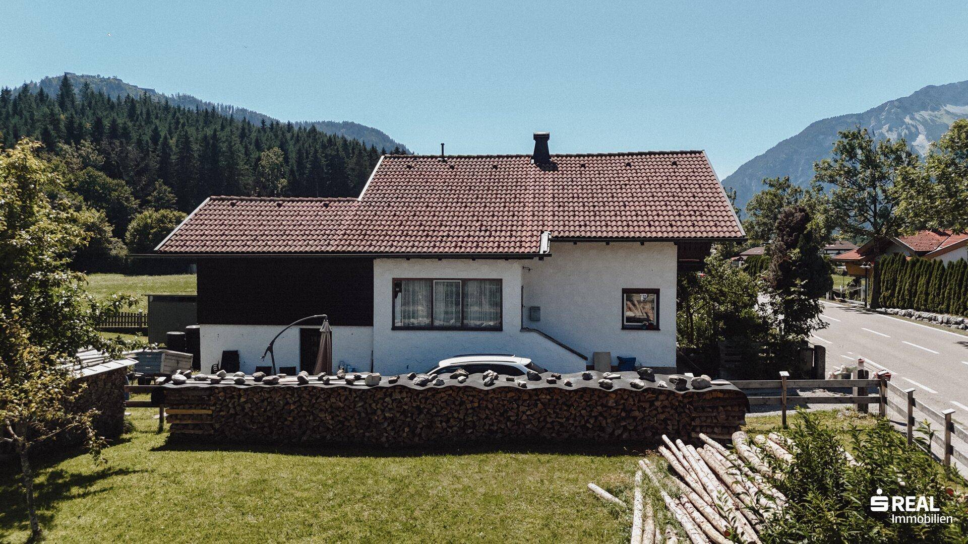 Vorderansicht des Hauses mit weißer Fassade, Fenstern und einem großen Holzstapel im Vorgarten.