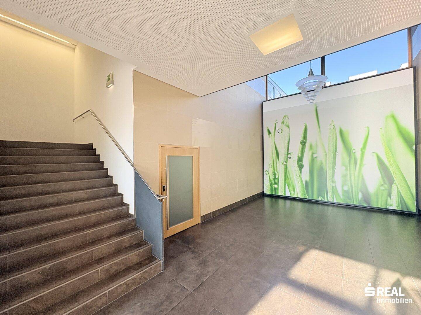 Modernes Treppenhaus mit dunklen Fliesen, Metallgeländer und einer dekorativen Wandgrafik.