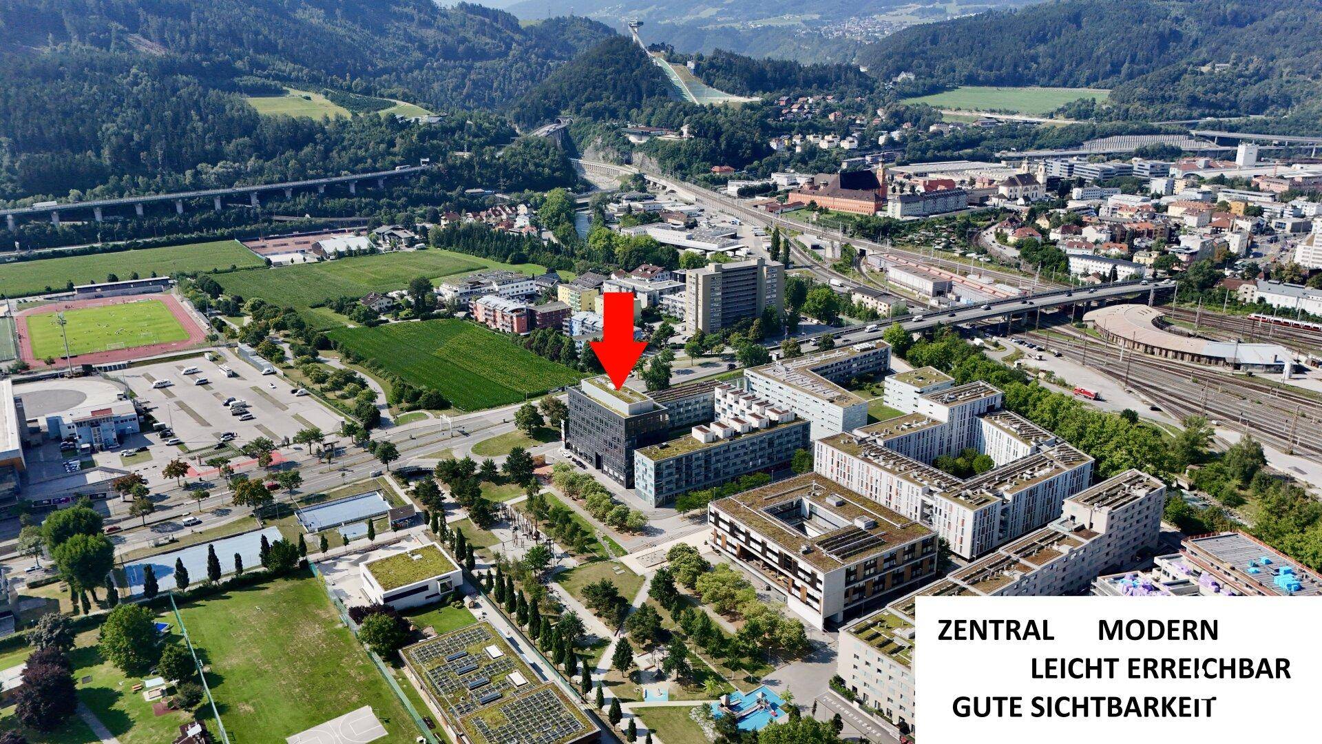 Weitläufige Luftaufnahme des Bürokomplexes in zentraler Lage mit umliegender Infrastruktur und Bergkulisse.