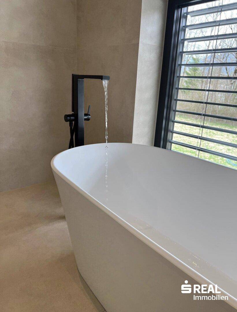 Modernes Badezimmer mit freistehender Badewanne und Wasserhahn, der Wasser einlaufen lässt.