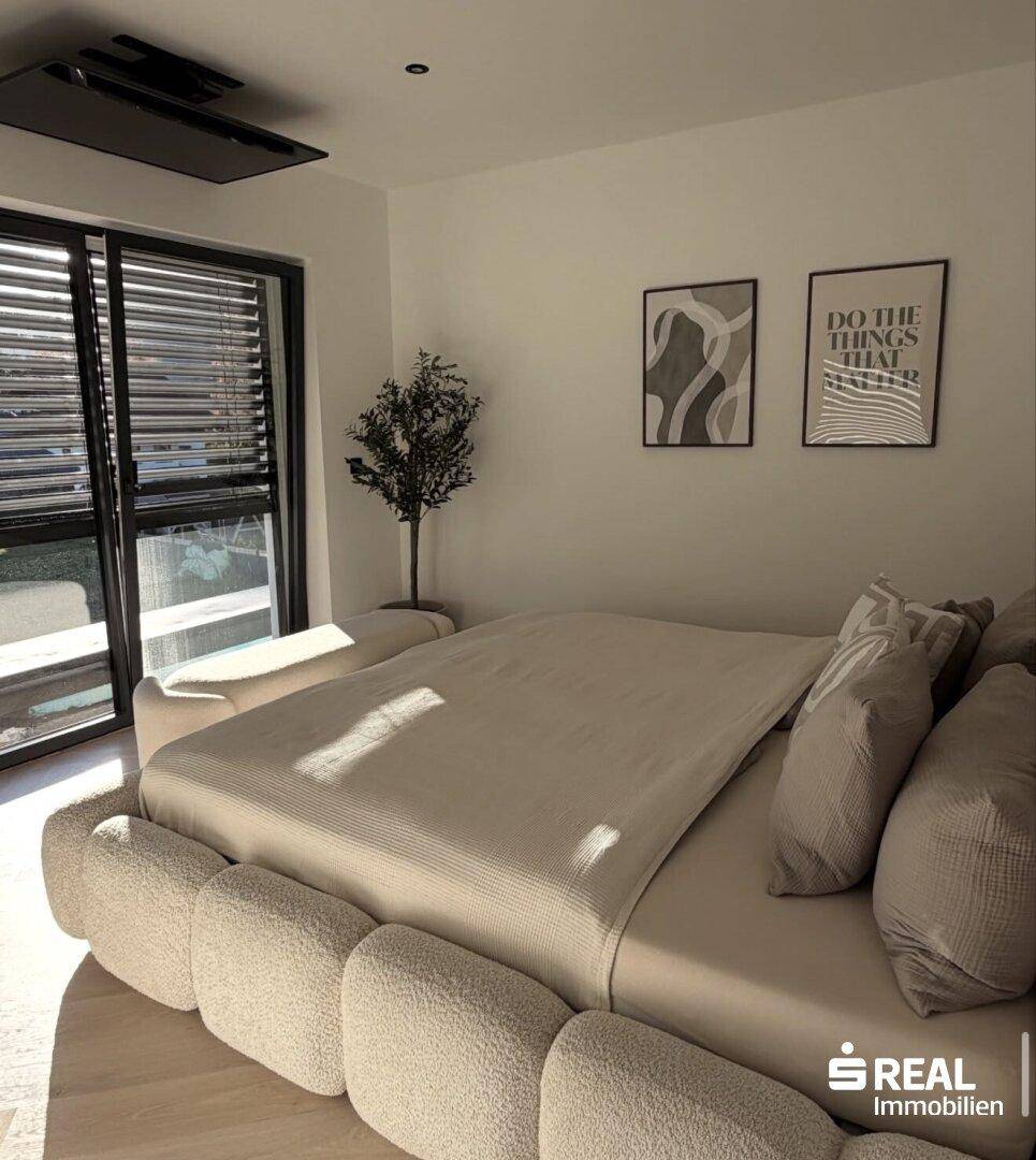 Modernes Schlafzimmer mit großem, gepolstertem Bett, minimalistischer Dekoration und viel Tageslicht.
