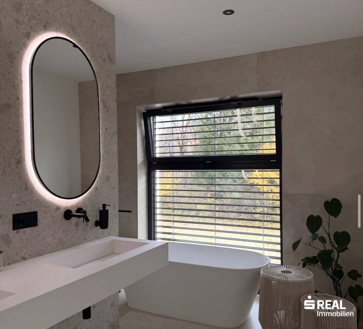 Elegantes Badezimmer mit freistehender Badewanne, beleuchtetem Spiegel und modernem Waschtisch.