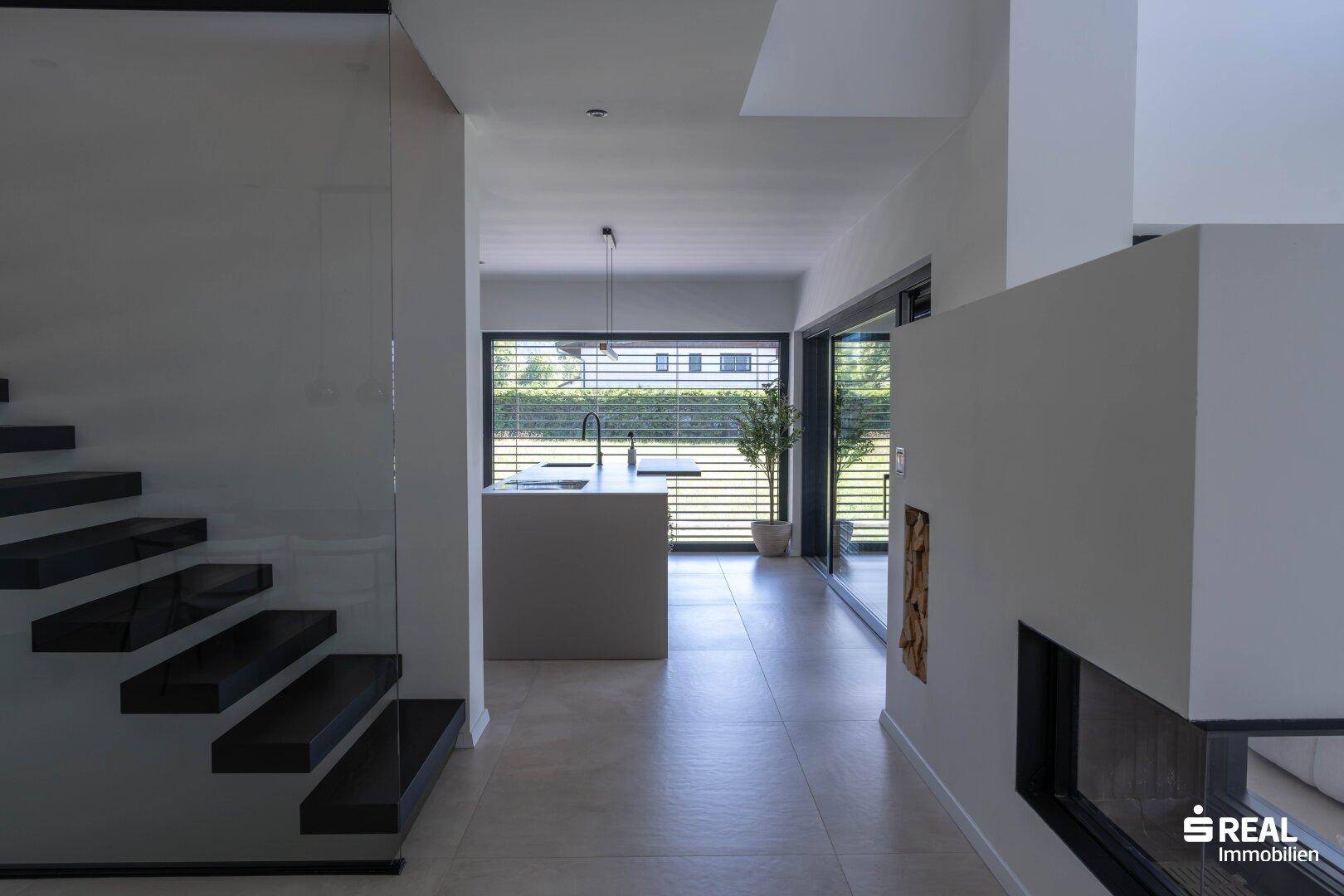 Heller Flur mit moderner Treppe, Blick auf die Küche und große Fensterfronten.