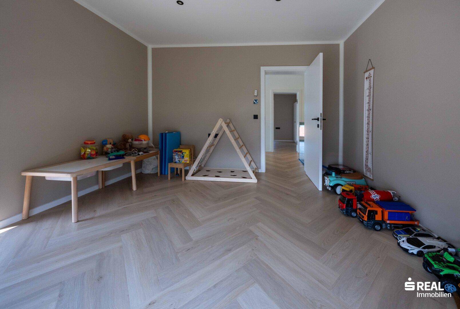 Kinderzimmer mit hellem Fischgrätparkett, Spielzeug und einem Holzklettergerüst.