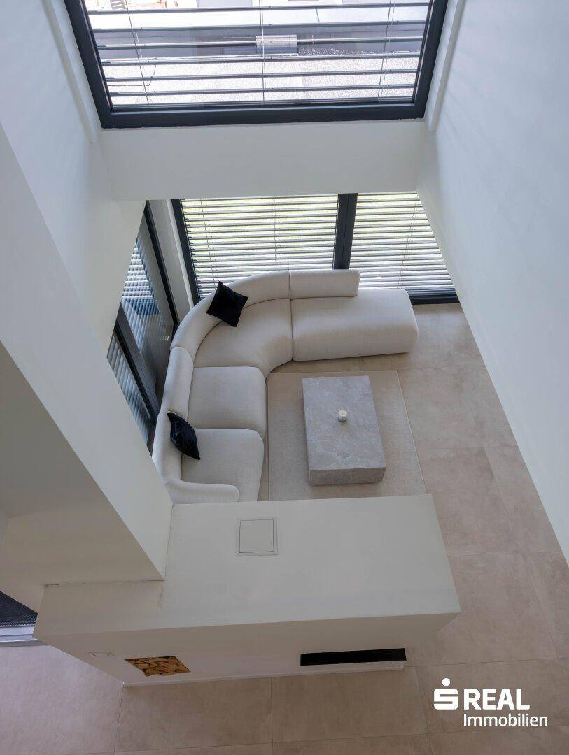 Blick von oben auf das helle Wohnzimmer mit großem Ecksofa, modernem Couchtisch und Kamin.