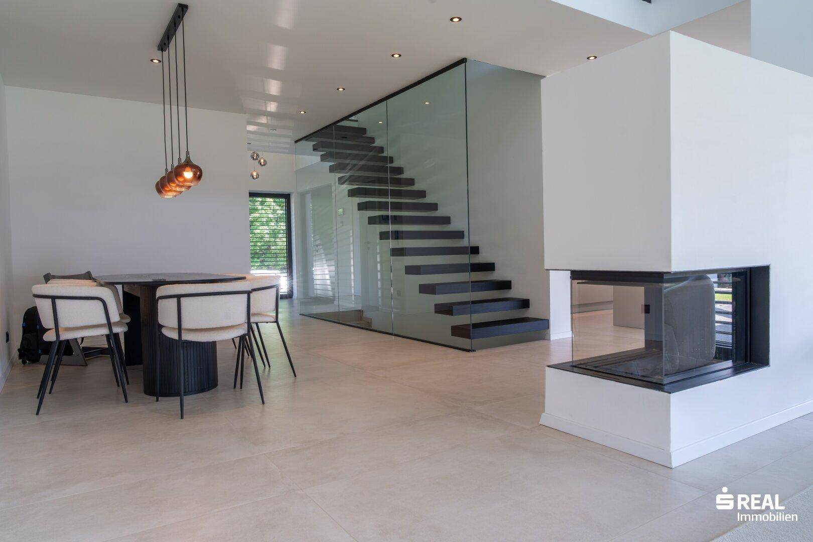 Offener Wohn- und Essbereich mit moderner Treppe, Esstisch und Kamin.