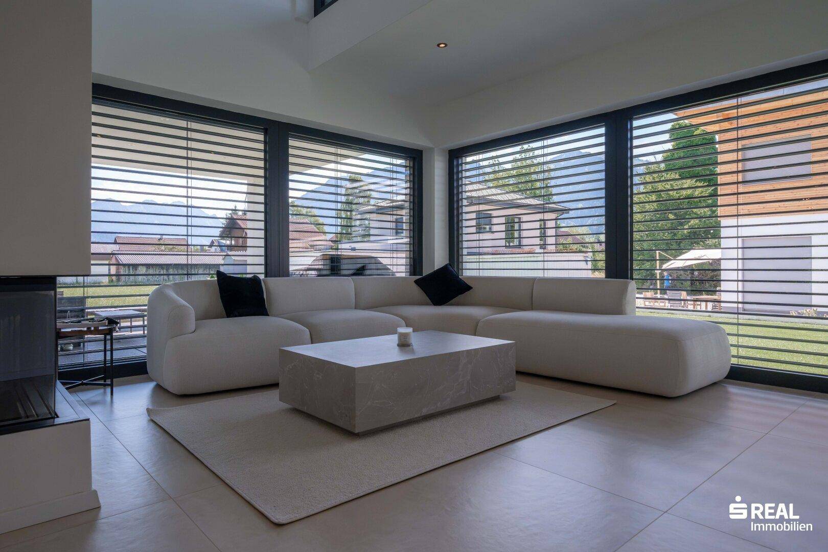 Helles Wohnzimmer mit großem Ecksofa, modernem Couchtisch und Blick auf die Berge und den Garten.