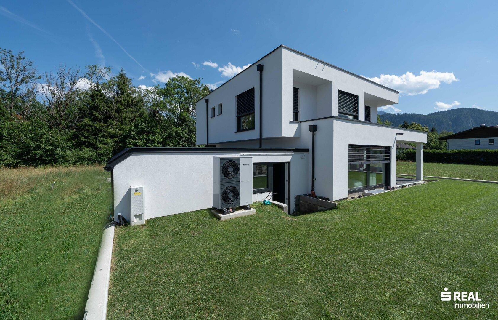 Modernes Haus mit Wärmepumpe und großem Rasenbereich unter blauem Himmel.
