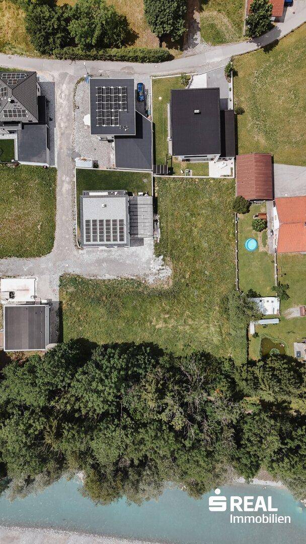 Luftaufnahme eines modernen Hauses mit Solaranlage und großem Grundstück am Fluss.