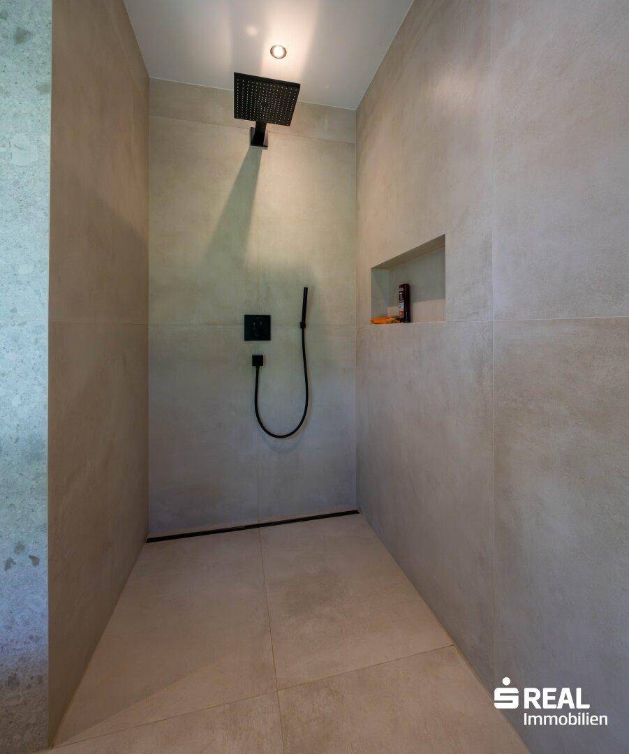 Modernes Badezimmer mit begehbarer Dusche, schwarzen Armaturen und großen Fliesen.