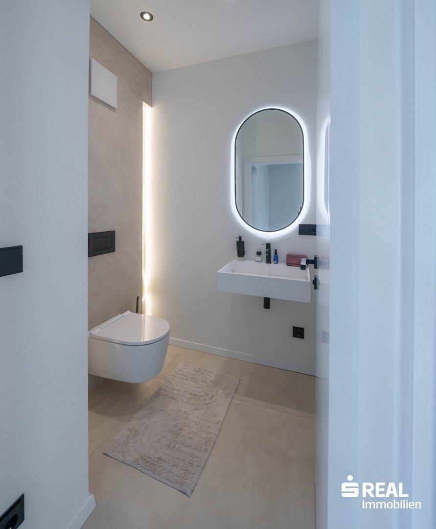 Modernes Gäste-WC mit beleuchtetem Spiegel, wandhängendem WC und minimalistischem Design.