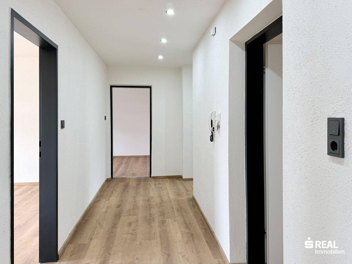 Heller Flur mit Laminatboden, weißen Wänden und modernen dunklen Türrahmen.