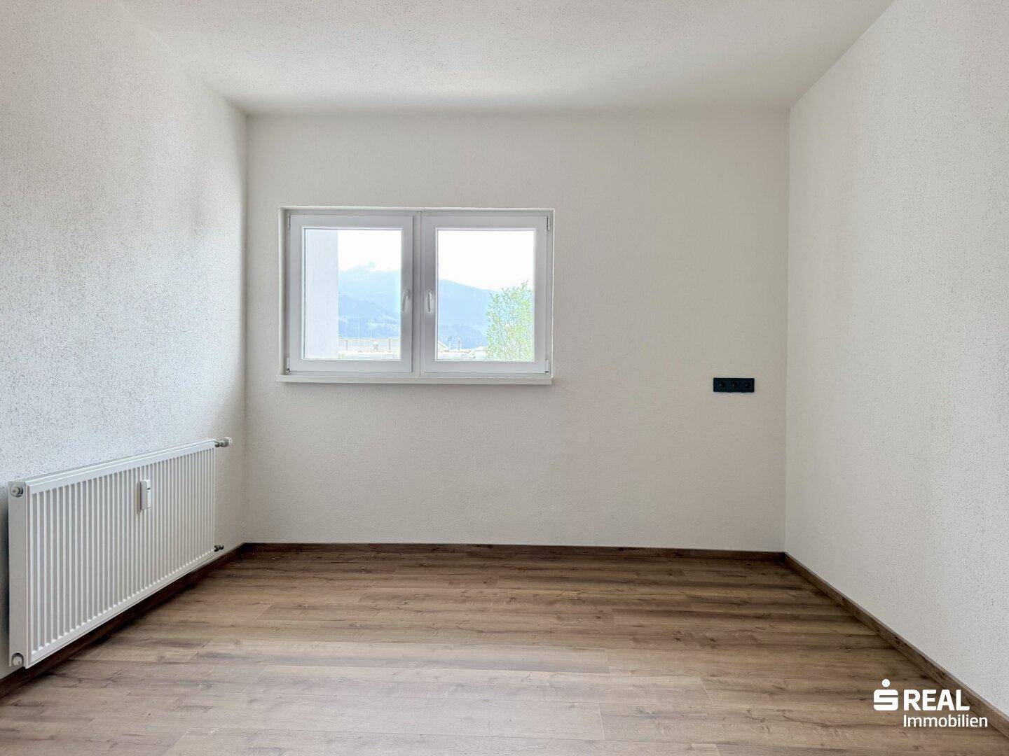 Helles, unmöbliertes Schlafzimmer mit Laminatboden, weiß gestrichenen Wänden und Bergblick.