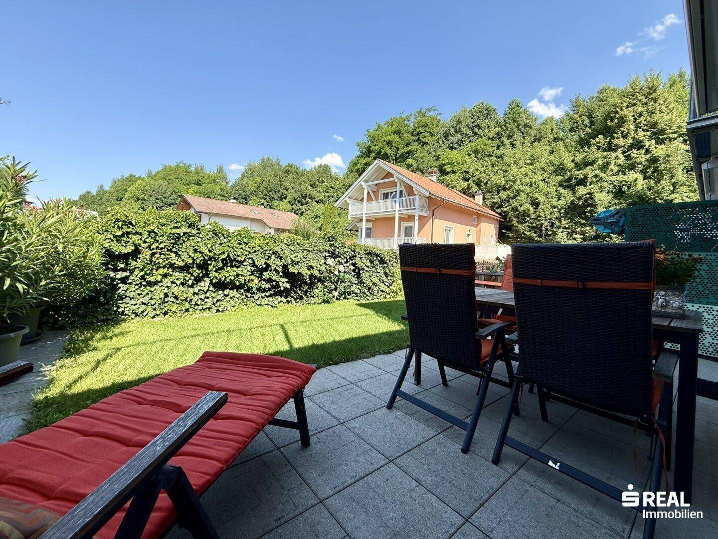 Sonniger Außenbereich mit Terrasse und Blick auf die umliegende grüne Landschaft und Häuser.