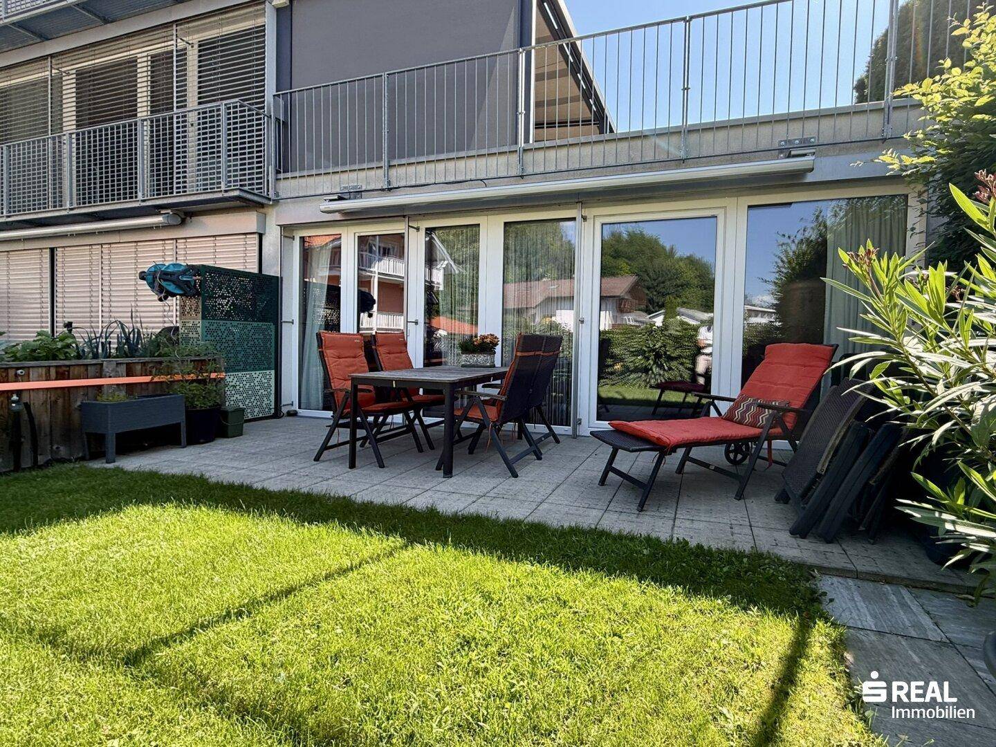 Großzügige Terrasse mit Rasenfläche und Gartenmöbeln, ideal für sonnige Tage und Mahlzeiten im Freien.