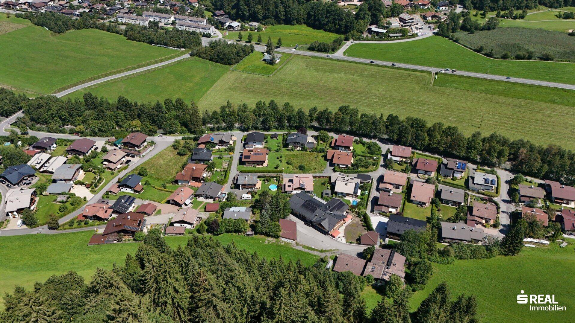 Weitläufige Luftaufnahme einer Wohnsiedlung, umgeben von grünen Feldern und Wäldern.