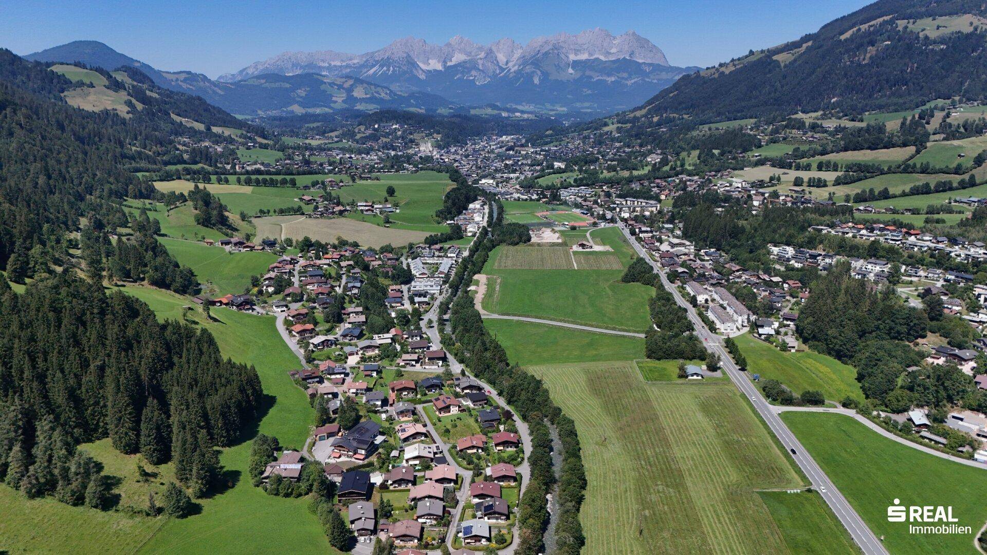 Panoramablick aus der Luft auf ein malerisches Tal mit einer Stadt, umgeben von Bergen und grünen Landschaften.