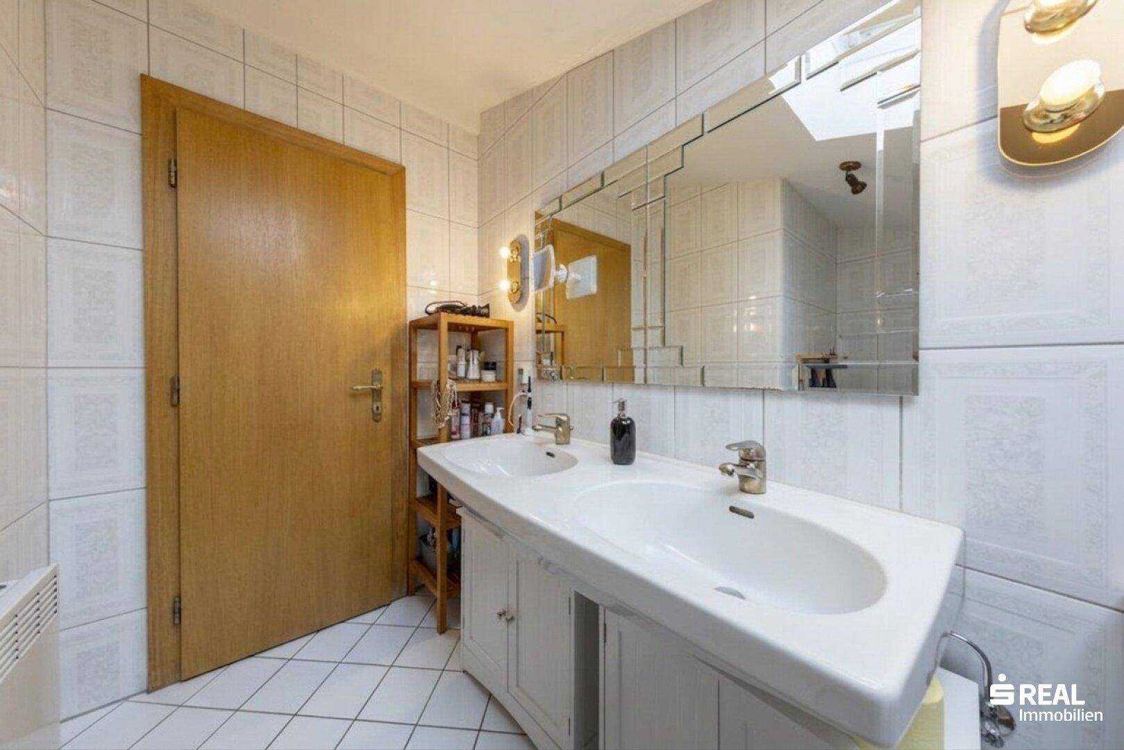 Helles Badezimmer mit Doppelwaschbecken, großem Spiegel und weißen Fliesen.