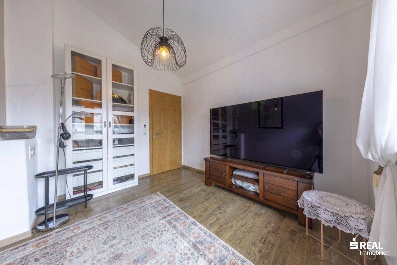 Helles Wohnzimmer mit großem Fernseher, modernem Hängesessel und Holzfußboden.