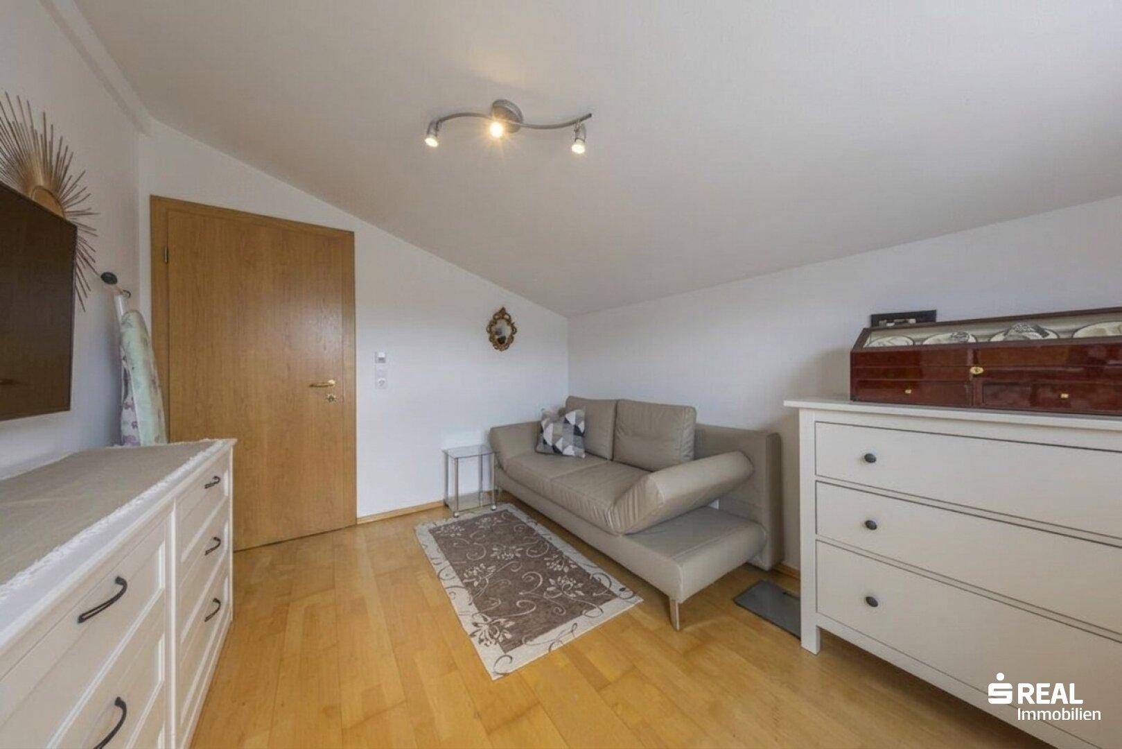 Gemütlicher Raum mit Dachschräge, Sofa und Holzfußboden, ideal als Gästezimmer oder Arbeitsbereich.