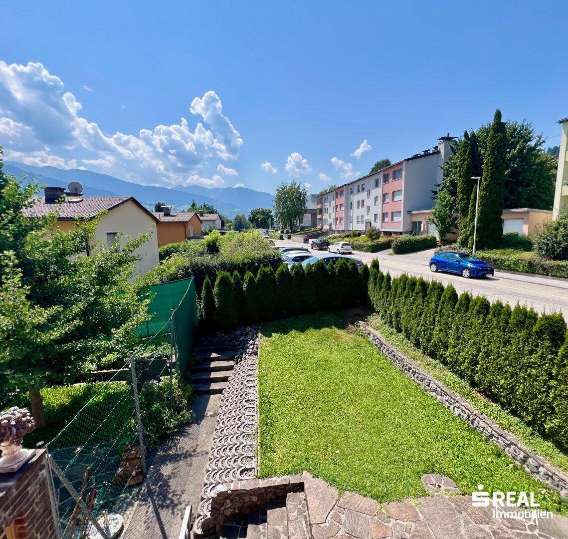 Garten mit Rasenfläche, Hecke und Blick auf die umliegende Landschaft und Berge.