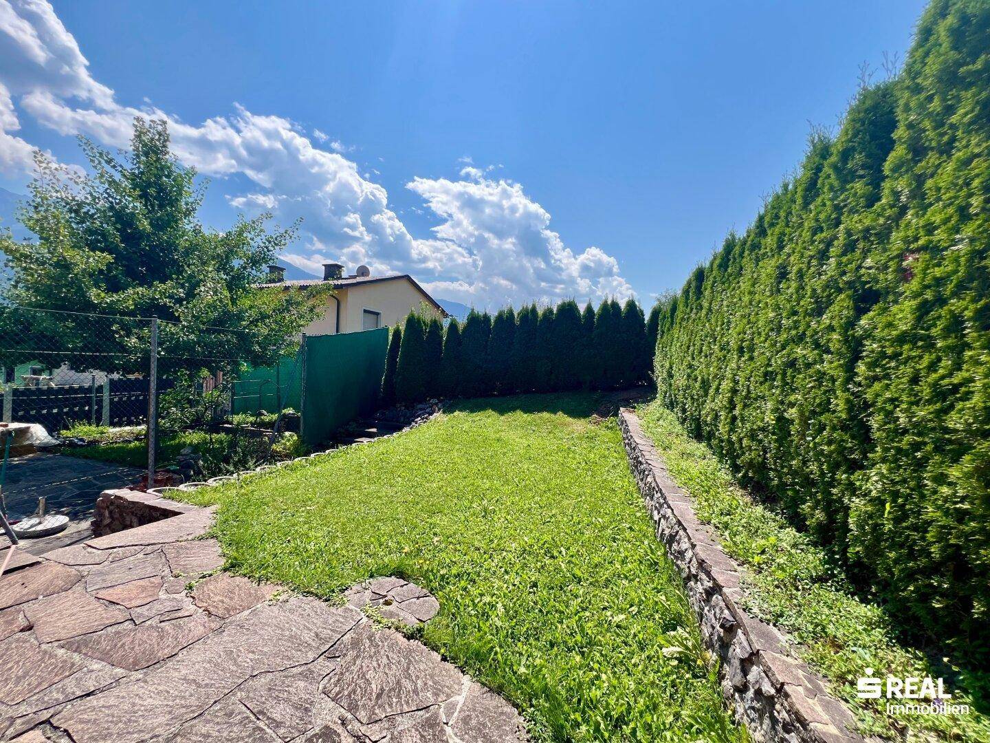 Gepflegter Gartenbereich mit Rasenfläche, Hecke und Steinplatten.