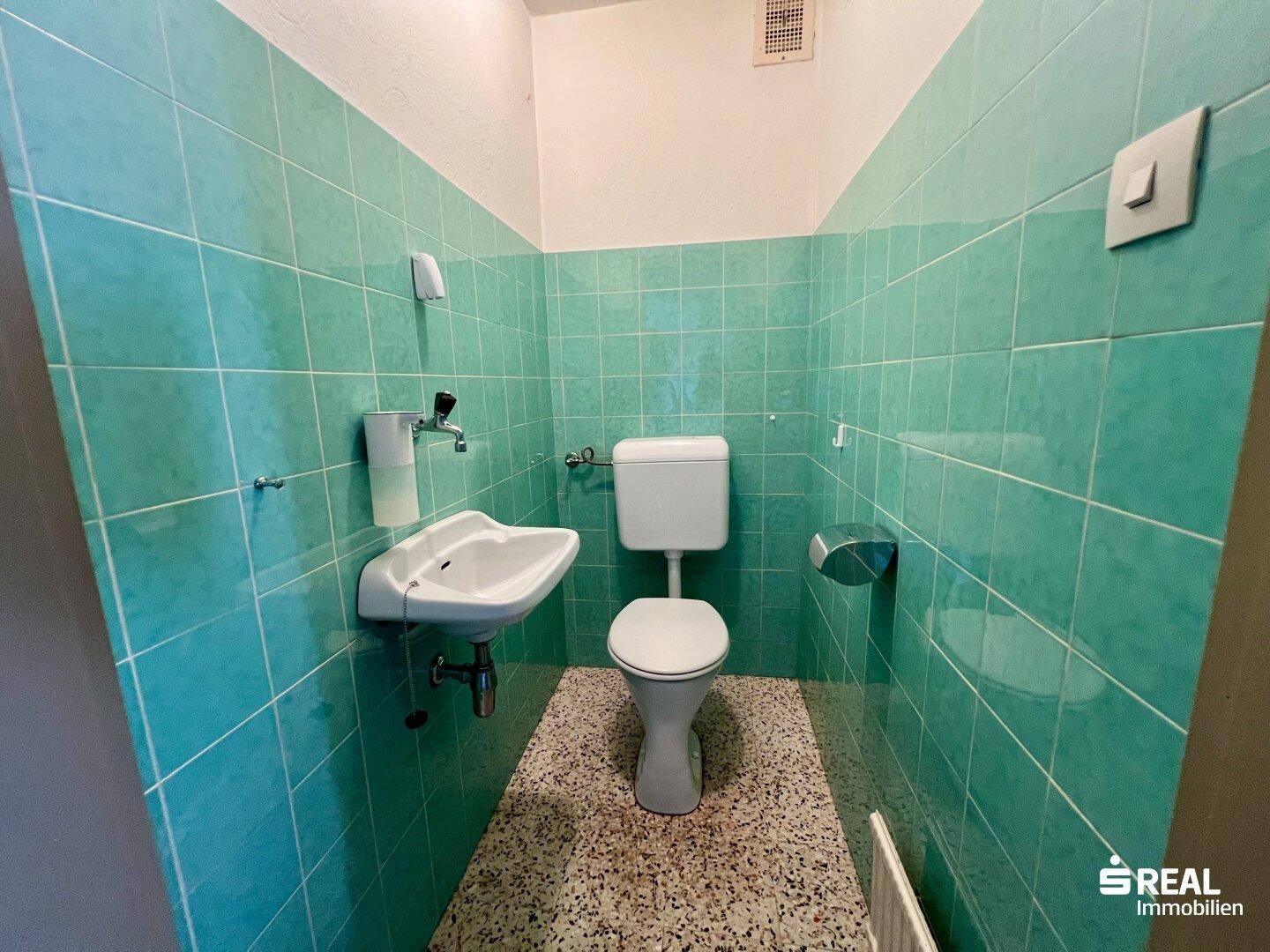 Separate Toilette mit türkisen Fliesen und kleinem Waschbecken.